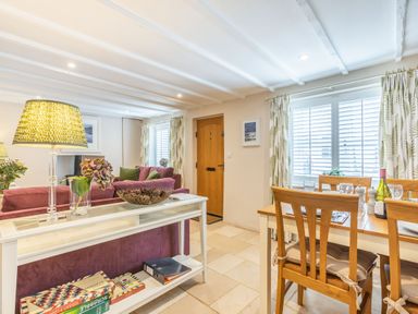 A living room and dining area with a wooden dining table and chairs a sofa a white console table with board games and a wooden door at Beach Retreat in Instow