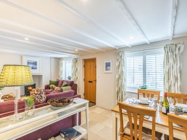 A living room and dining area with purple sofas a wooden dining table and chairs a glass table lamp and a wooden door at Beach Retreat in Instow
