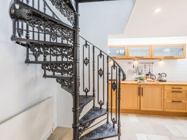 A black ornate metal spiral staircase next to a wooden kitchen counter with utensils hanging at Beach Retreat in Instow