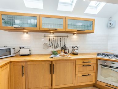 A kitchen with wooden cabinets countertop microwave toaster kettle stove and kitchen utensils on a rack at Beach Retreat in Instow