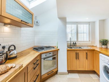 A kitchen with wooden cabinets a gas stove an oven a double sink a washing machine and a window with shutters at Beach Retreat in Instow