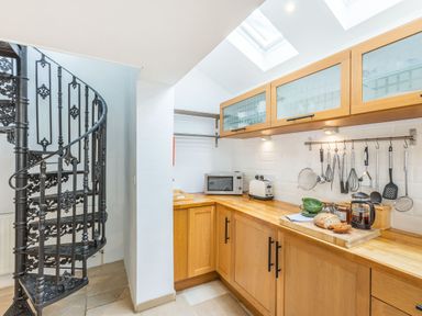 A kitchen with wooden cabinets a black spiral staircase and kitchen utensils on hooks at Beach Retreat in Instow