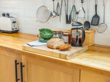 A kitchen counter with sliced bread on a cutting board next to a French press and green cups at Beach Retreat in Instow