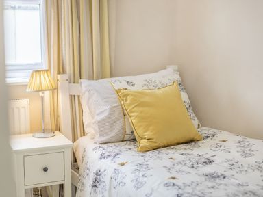 A bedroom with a single bed with floral bedding and a yellow pillow next to a white nightstand with a lamp at Beach Retreat in Instow