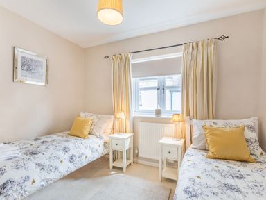 A bedroom with two single beds bedside tables lamps and a window with curtains at Beach Retreat in Instow