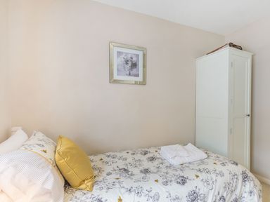 A bedroom with a single bed with floral bedding and pillows a white wardrobe and a framed picture on the wall at Beach Retreat in Instow