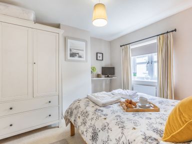 A bedroom with a bed a wardrobe a window with curtains and a small desk with a computer at Beach Retreat in Instow