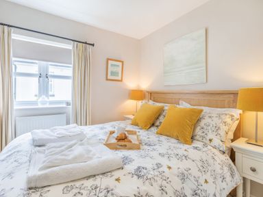 A bedroom with a bed with floral bedding and yellow pillows and two bedside tables with lamps at Beach Retreat in Instow