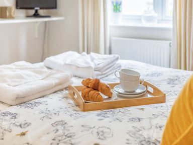 A bed with a floral duvet holding a wooden tray with croissants and stacked cups at Beach Retreat in Instow
