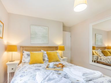 A bedroom with a wooden bed frame yellow pillows floral bedding bedside tables with lamps and a large mirror on the wall at Beach Retreat in Instow