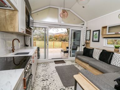 A kitchen and living area with patterned floor tiles a gray sofa and sliding glass doors leading to a wooden deck at Meadow Retreat in Nantmel near Rhayader
