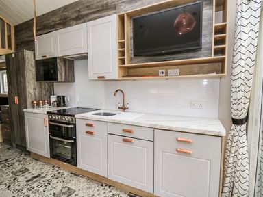 A kitchen with white cabinets copper handles a stove oven microwave sink and a wall mounted television at Meadow Retreat in Nantmel near Rhayader