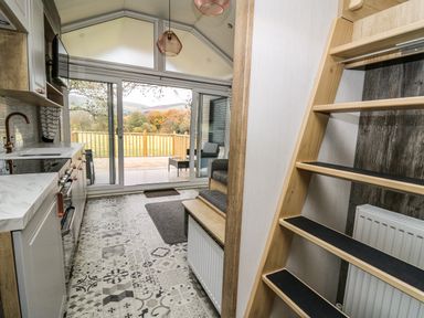 A kitchen with patterned tile floor shelves and sliding glass doors opening to a deck at Meadow Retreat in Nantmel near Rhayader