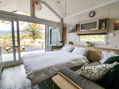 A bedroom with a bed sofa window and sliding glass doors overlooking an outdoor area at Meadow Retreat in Nantmel near Rhayader