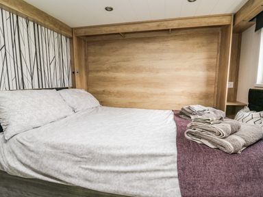 A bedroom with a bed covered in white bedding and folded towels on a purple blanket at Meadow Retreat in Nantmel near Rhayader