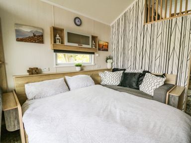 A bedroom with a bed and sofa with cushions near a window and patterned wallpaper at Meadow Retreat in Nantmel near Rhayader