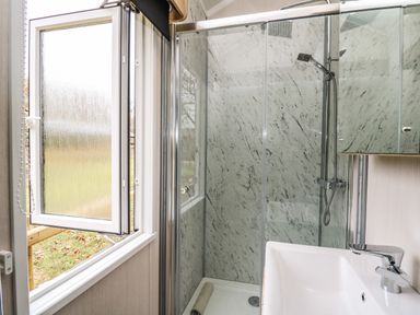 A bathroom with a shower enclosure a washbasin and an open window at Meadow Retreat in Nantmel near Rhayader