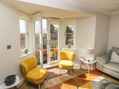 A living room corner with two yellow chairs a small white table with a lamp and a gray sofa at Seashells in Tenby