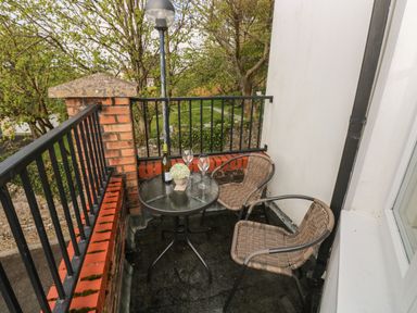 A small balcony with two wicker chairs a round glass table holding a wine bottle two glasses and a small plant at Seashells in Tenby