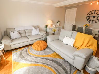 A living room with two gray sofas a yellow throw and knitted cushion a patterned rug and a glass dining table at Seashells in Tenby
