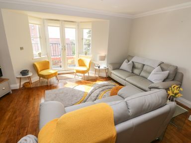 A living room with two yellow chairs by glass doors and two grey sofas at Seashells in Tenby