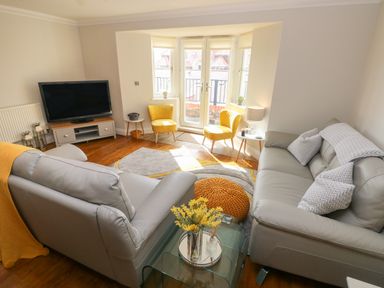 A living room with two gray sofas yellow chairs a TV on a stand and large windows at Seashells Tenby
