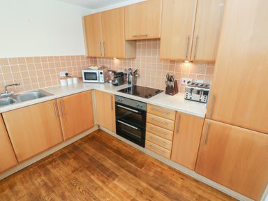 A kitchen with wooden cabinets a double sink an oven a cooktop a microwave a toaster and a knife block at Seashells in Tenby