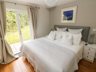 A bedroom with a bed white bedding bedside tables lamps and patio doors leading to a garden at Seashells in Tenby