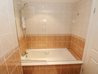 A bathroom with a bathtub shower faucet and tiled walls at Seashells in Tenby
