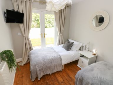 A bedroom with two single beds gray blankets curtains on glass doors and a wall-mounted TV at Seashells in Tenby