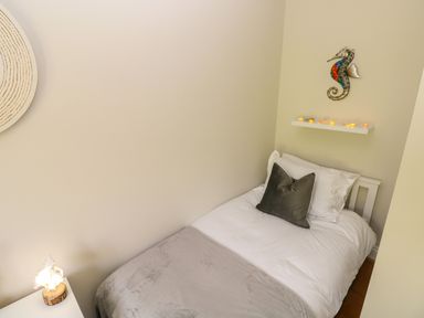 A small bedroom with a single bed white bedding grey blanket and a dark grey pillow a seahorse wall decoration and a shelf with small lights at Seashells in Tenby