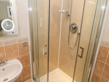 A bathroom with a shower enclosure with glass doors a sink and a wall-mounted mirror at Seashells in Tenby