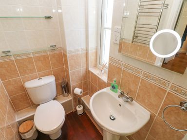 A small bathroom with a toilet sink mirror and window at Seashells in Tenby