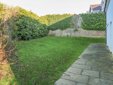 A garden with grass and a paved pathway next to a building with a wall covered in ivy at Seashells in Tenby