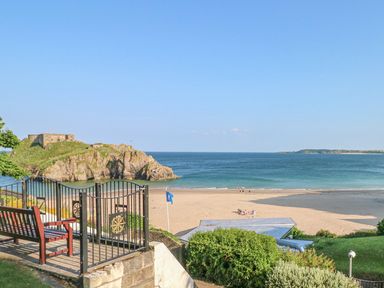 A beach with people on the sand a rocky outcrop with a building and a blue flag near the shore at Seashells in Tenby