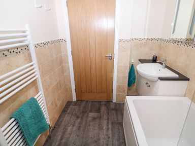 A bathroom with a wooden door a white sink and cabinet a bathtub and a towel rack with a turquoise towel at Elliotts Retreat in Sheringham