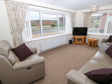 A living room with two leather sofas a television on a wooden stand and beige curtains at Elliotts Retreat in Sheringham