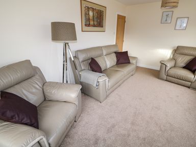 A living room with grey leather sofas a floor lamp and framed pictures on the wall at Elliotts Retreat in Sheringham