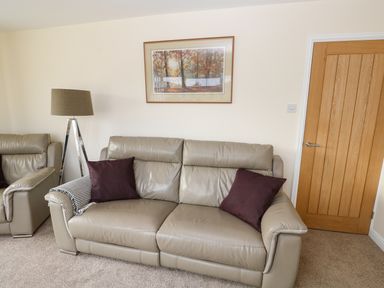 A living room with leather sofas a floor lamp a framed picture on the wall and a wooden door at Elliotts Retreat in Sheringham