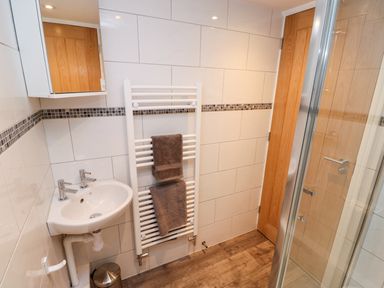 A bathroom with a corner sink a towel warmer with two towels a wooden door and a glass shower door at Elliotts Retreat in Sheringham