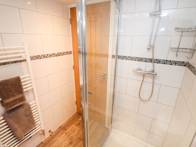 A bathroom shower area with tiled walls a glass door a showerhead and a white towel rack with towels at Elliotts Retreat in Sheringham