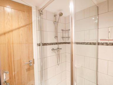 A shower area with glass door tiled walls and a wooden door at Elliotts Retreat in Sheringham