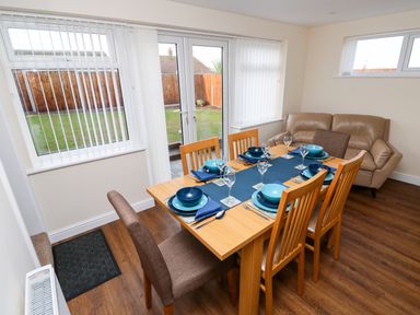 A dining area with a wooden table set with blue dishes and glasses next to a beige sofa at Elliotts Retreat in Sheringham