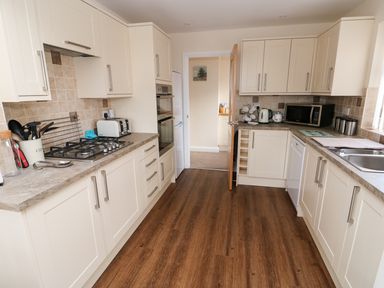 A kitchen with white cabinets and wooden floor at Elliotts Retreat in Sheringham