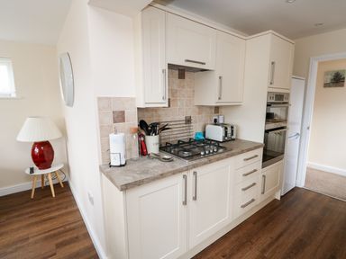 A kitchen with white cabinets a gas stove a toaster and cooking utensils next to a side table with a red lamp at Elliotts Retreat in Sheringham