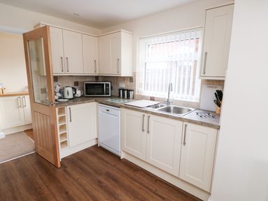 A kitchen with white cabinets a dishwasher a microwave a kettle and a double sink at Elliotts Retreat in Sheringham