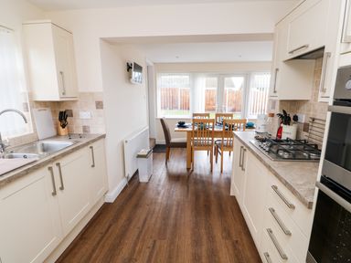 A kitchen with white cabinets and a dining table with chairs near windows at Elliotts Retreat in Sheringham