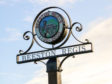 A metal signpost with the name Beeston Regis and a circular emblem illustrating a building and landscape