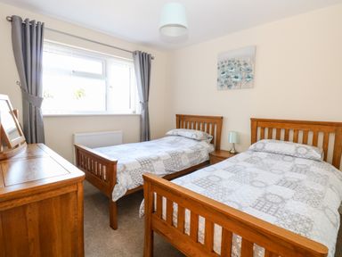 A bedroom with two wooden single beds a wooden dresser grey curtains and a window at Elliotts Retreat in Sheringham
