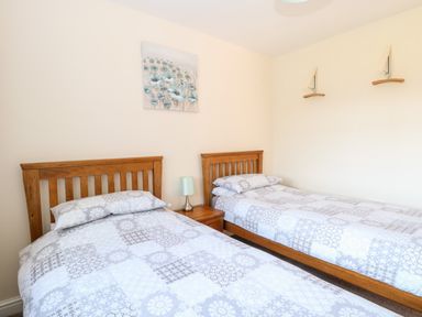 A bedroom with two single beds wooden headboards a nightstand with a lamp and wall decorations at Elliotts Retreat in Sheringham